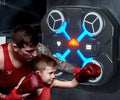 A child practicing with a TU SHOP boxing machine for kids while a trainer assists.